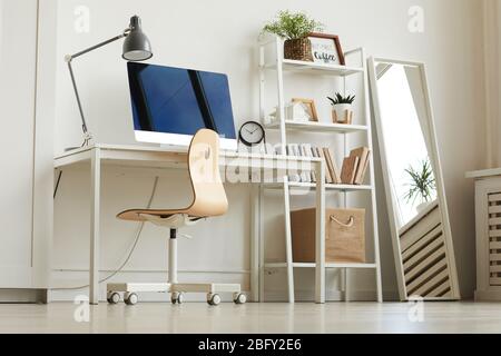 Low angle view at all-white home office workplace with wooden chair and modern computer on desk, copy space Stock Photo