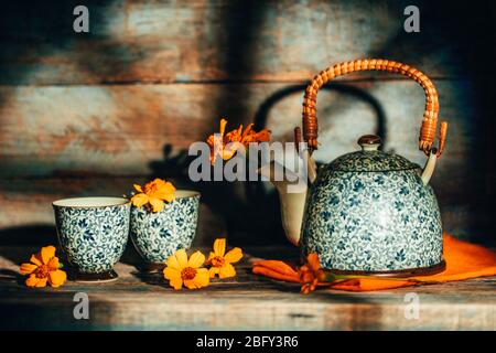 Stiil life with Chernobrivtsi flowers in vintage teapot and cups on rustic old background with sunset light from the window. Stock Photo
