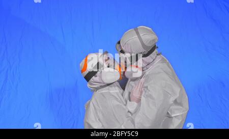 Doctor man and woman in protective costume suit, gas protect medical spray paint mask. Love couple kiss and hug, health worker in respirator Covid-19. Stock Photo