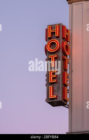 Neon hotel sign on the building corner against the sunset sky Stock Photo