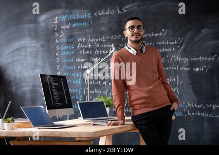 Portrait of bearded Arabian software developer with wireless headphones around neck standing at desk with computers in office Stock Photo