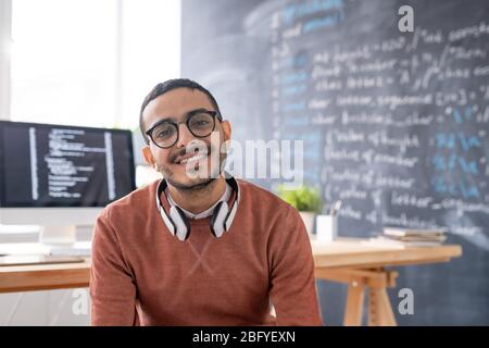 Portrait of smiling young Arabian programmer in eyeglasses sitting in modern office of IT company Stock Photo