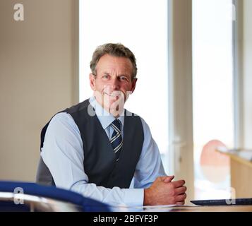 Portrait of a successful businessman sitting at his work desk looking at camera and smiling Stock Photo