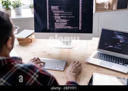 Over shoulder view of system programmer sitting at wooden table and providing network security in office Stock Photo