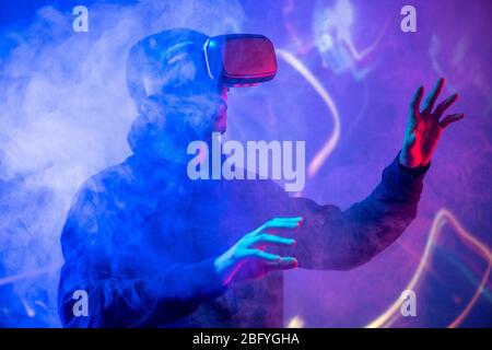 Young Arabian man using virtual reality device gesturing hands in smoked VR room Stock Photo