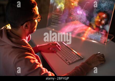 Over shoulder view of young engineer in glasses sitting at table and designing 3D model on computer Stock Photo