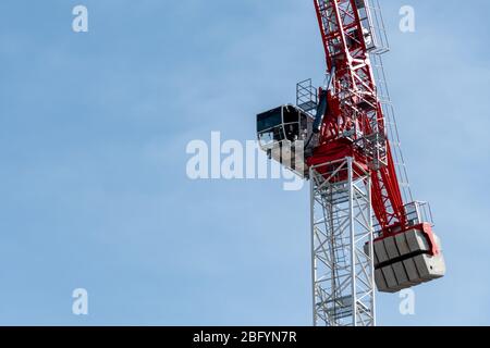Close-up of the operator cabin of a red and white tower crane against a blue sky. Stock Photo