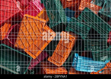 Old plastic boxes in a warehouse as a trash behind the metal mesh fence. Stock Photo