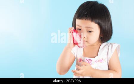 Cute Asian girls are using ice bags. Apply on the cheek to reduce toothache, sore, swelling from tooth decay and oral problems. On a blue background a Stock Photo