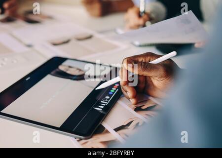 Close-up of a man working on digital tablet on meeting table. Processing photos on a tablet computer for their project in a meeting. Stock Photo