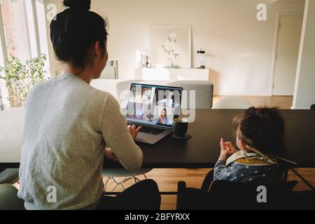 Woman working from home, with her daughter sitting by at the table, having a video conference call. Businesswoman having a video conference call from Stock Photo