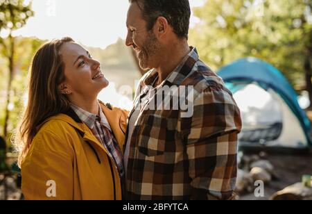 Affectionate couple looking at each other and smiling. Loving couple standing at their campsite with tent in background. Stock Photo