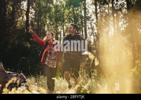 Couple hiking through forest trails. Woman showing something to man while walking towards their camping site. Stock Photo