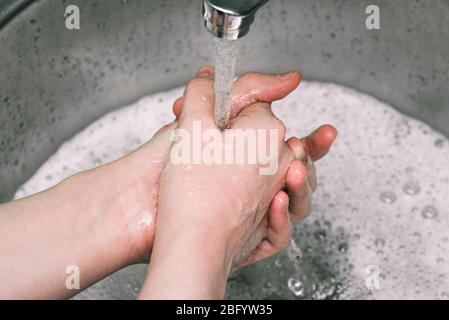Woman washing hands in sink. Prevent spread of virus, wash your hands regularly with soap. Water running from faucet. Washing hands rubbing with soap Stock Photo