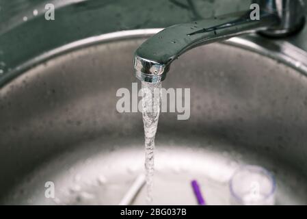 Water drop from faucet in the kitchen. Water from the tap. A stream of clean water flows into the sink. Open chrome faucet washbasin Stock Photo