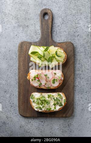 Sandwiches with sundries tomatoes, fresh radish microgreens, cream cheese on chopping board on grey background. Top view. Vertical format. Stock Photo