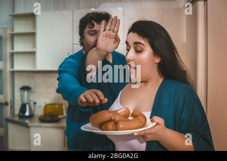 Big man wants to grab sausage from his wife's plate Stock Photo