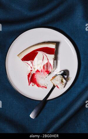 Creative minimalist food photography, strawberry cheesecake on a white plate with spoon over dark blue background.