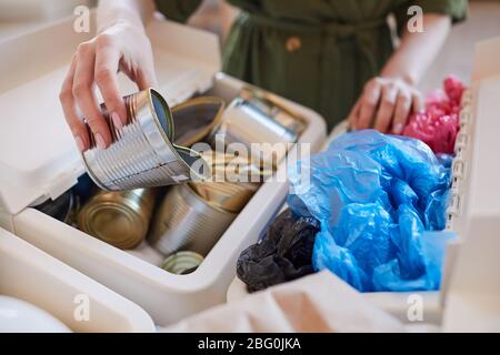 Close up of unrecognizable woman putting discarded metal cans into trash bin while sorting waste at home, copy space Stock Photo