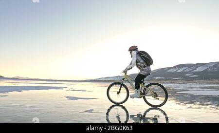 Woman is riding bicycle on the ice. Tires on bike are covered wi