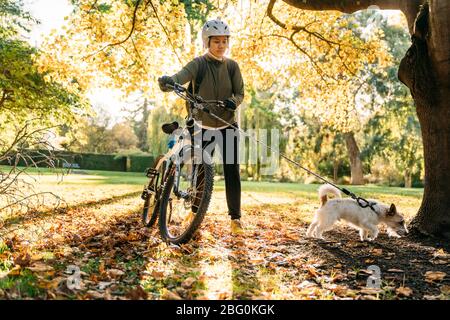 19/4/2020 Asian woman with a bike walking with a dog in autumn at the Botanic garden, Oamaru, New Zealand. Concept about exercise while social isolati Stock Photo