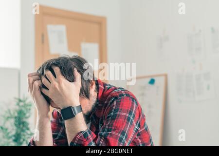 Disappointed freelancer at home office with his head in hands, selective focus Stock Photo