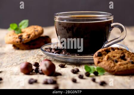 Black coffee in a glass cup with coffee beans. near cookies and hazelnuts Stock Photo