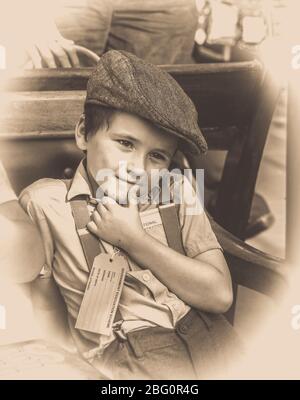 Old fashioned, vintage sepia close up portrait of evacuee child, WW2 boy in flat cap & braces at vintage railway station, 1940s WWII summer event, UK. Stock Photo