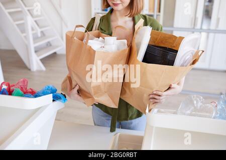 Mid section portrait of modern young woman holding paper bags with plastic items while sorting waste at home, copy space Stock Photo