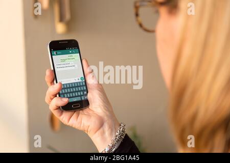 Senior woman with smartphone in her hands and a whatsapp conversation on the screen. Stock Photo