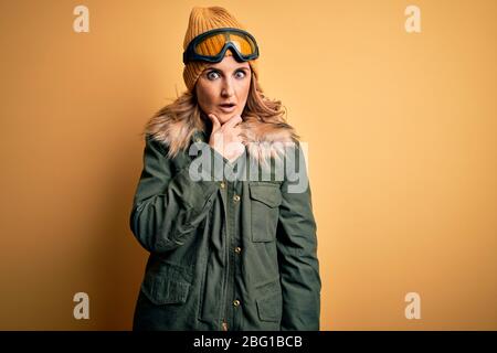 Middle age beautiful blonde skier woman wearing snow sportwear and ski goggles Looking fascinated with disbelief, surprise and amazed expression with Stock Photo