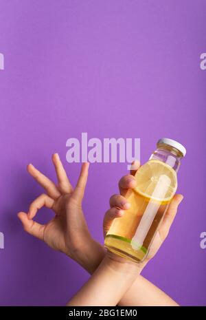 Woman showing ok and bottle of detox water infused with sliced raw lemon Stock Photo