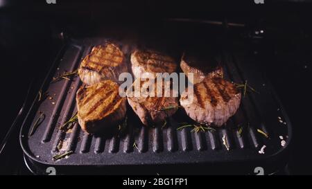 Delicious juicy meat steak cooking on grill. Prime beef fry on electric roaster, rosemary, black pepper, salt. Slow motion. Stock Photo