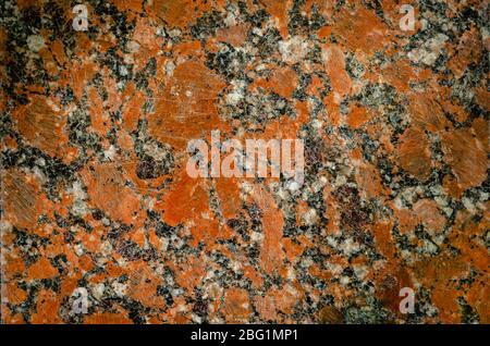 Red granite background. The texture of the old granite. Red polished granite with scratches and cracks. The texture of natural stone. Close-up. Stock Photo