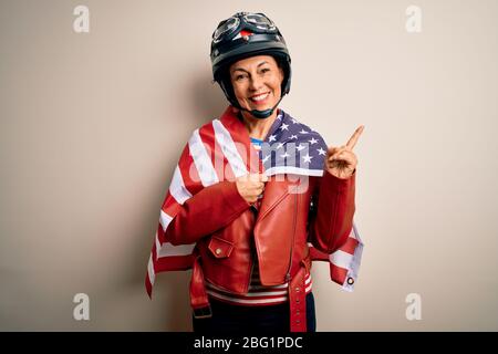 Middle age motorcyclist woman wearing motorcycle helmet and united states flag very happy pointing with hand and finger to the side Stock Photo