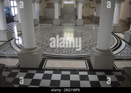 A grand museum hall hallway featuring marble columns, a checkerboard entryway, and a large circular mosaic tile floor. Stock Photo