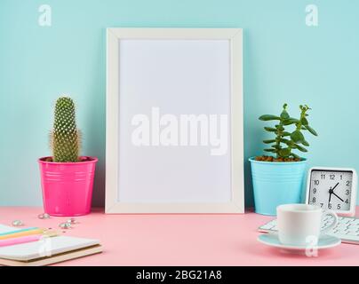 Mockup with blank white frame, alarm, notepad, cup of coffee or tea on pink table Stock Photo