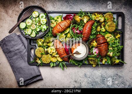 Baked vegetables salad with tahini dressing on cast-iron pan. Baked sweet potato, broccoli and zucchini with arugula. Healthy vegan food concept. Stock Photo
