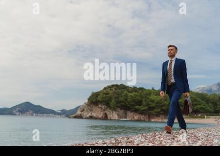 Businessman walking on the beach holding in hand briefcase Stock Photo