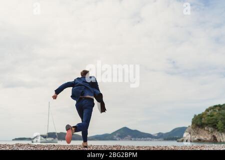 Businessman running to the sea holding in hand briefcase. Back view Stock Photo
