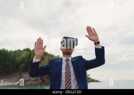 Businessman uses VR-headset to display a virtual reality on a background of sea Stock Photo