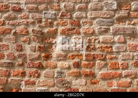 Old brick wall background texture with different tones of red and different stone shapes, illuminated by the sun Stock Photo