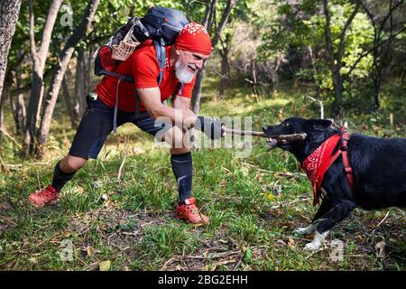 Bearded man in red shirt playing with dog. Outdoor travel concept Stock Photo