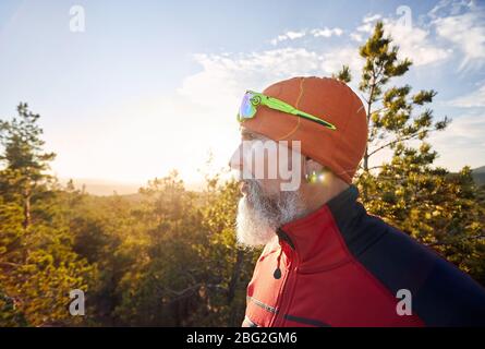 Portrait of old man with white beard in red shirt and in the forest at sunset Stock Photo