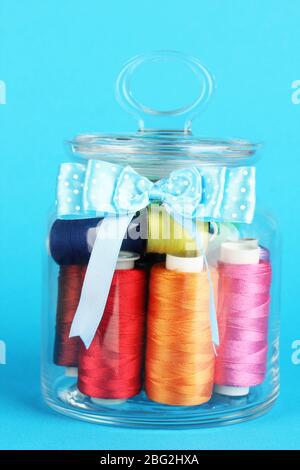 Sewing thread, glass jar and blue background for craft, tailor or ...