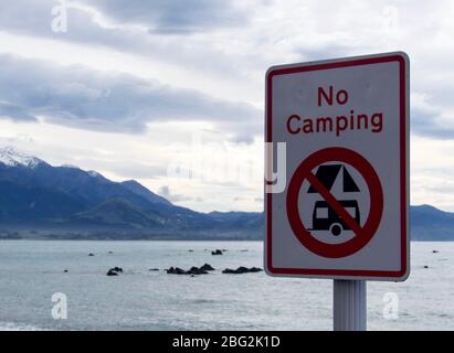 'No Camping' sign along the Esplanade in Kaikoura with mountains and beach in backdrop Stock Photo