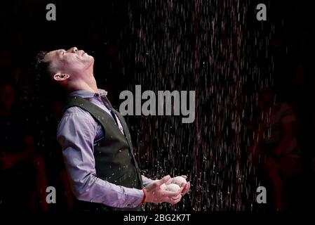 A performer in the Cambodian Phare Circus standing below a shower of rice Stock Photo