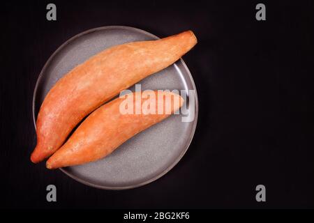 Raw sweet potatoes on the black background. Top view Stock Photo
