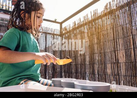 child with a shovel putting soil in the balcony pots before planting, hobbies at home, sustainable and ecological lifestyle concept Stock Photo
