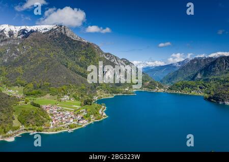 The Improbable aerial landscape of village Molveno, Italy, azure water of lake, empty beach, snow covered mountains Dolomites on background, roof top Stock Photo